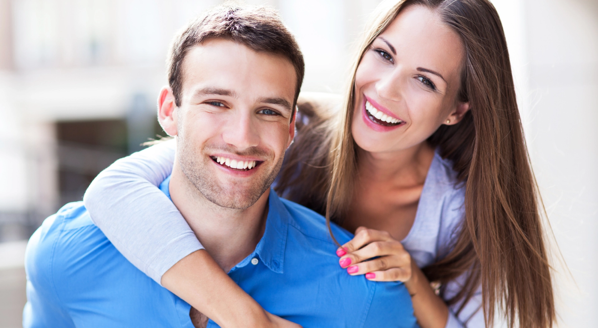Young couple smiling at camera in casual indoor setting, wearing blue shirt.